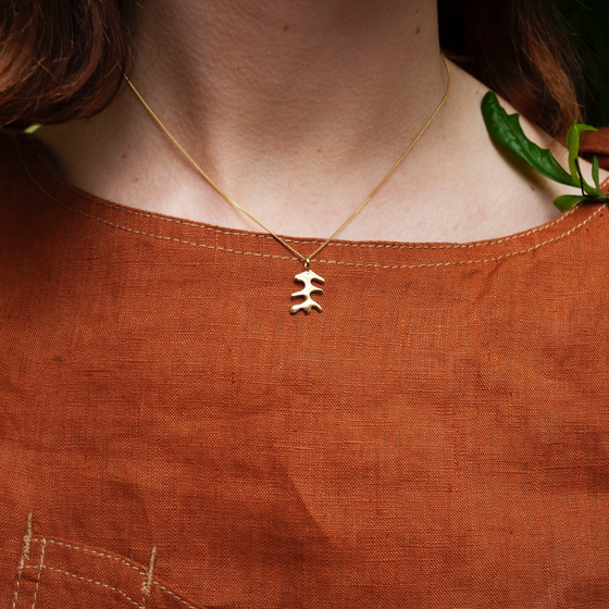 Woman wearing pendant necklace with a gold abstract shape charm on it