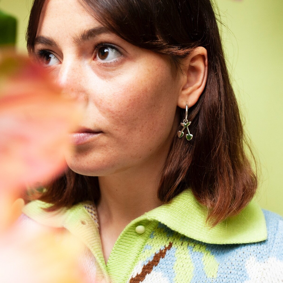 Woman wearing small hoop earring with a cherry charm hanging from it