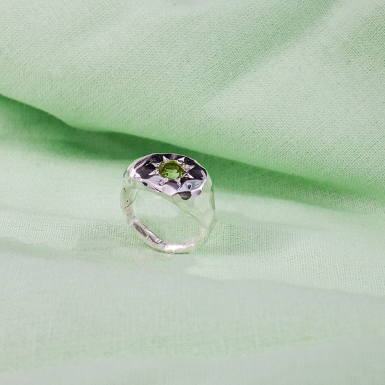 Silver signet ring with a pale green gen in the centre, surrounded by a sun shape