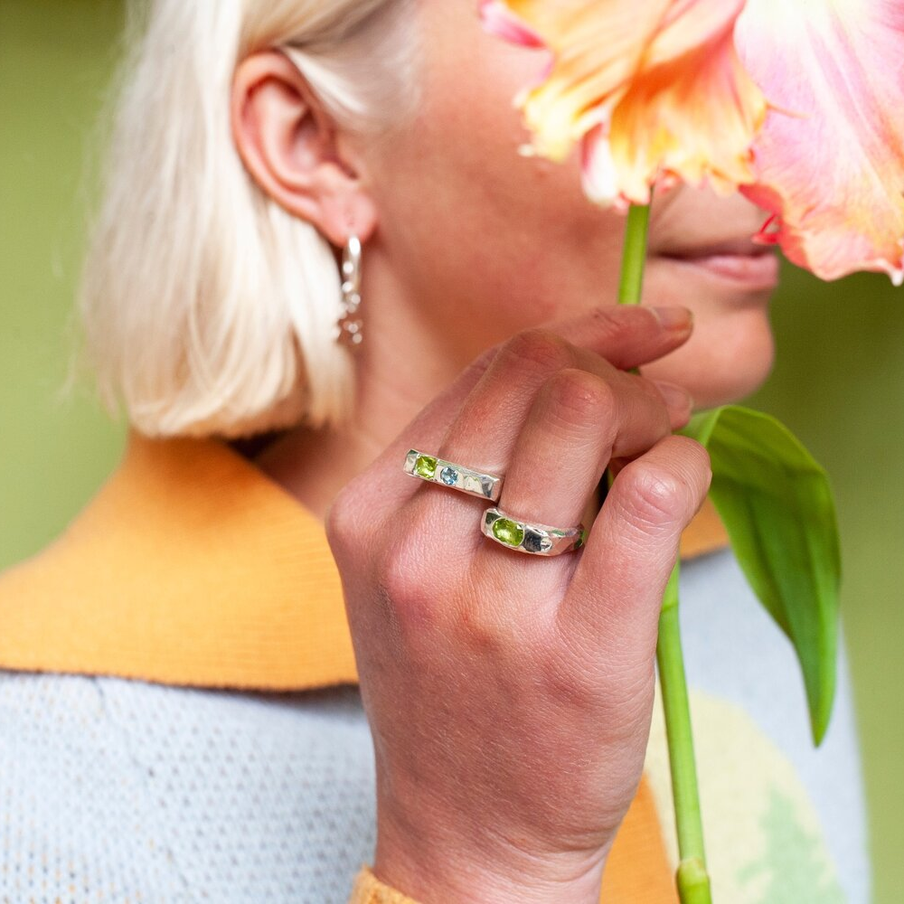 Close up of hand wearing a silver ring with a green gem and a blue gem inset into it