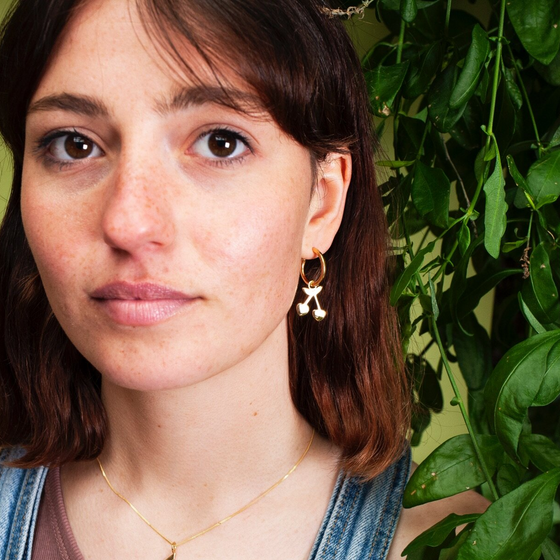 Close up of woman wearing small hoop earring with a cherry charm hanging from it