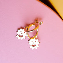  Close up of small hoop earrings with an irregular spikey shaped charm with a smiling face on