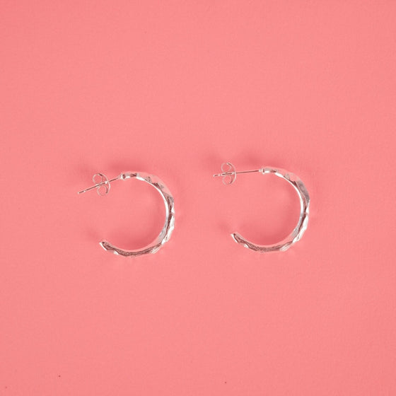 Close up of small silver hoop earrings with a textured surface