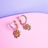 Close up of small hoop earrings with an irregular spikey shaped charm with a smiling face on
