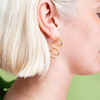 Close up of woman wearing gold earring in the shape of a squiggle.