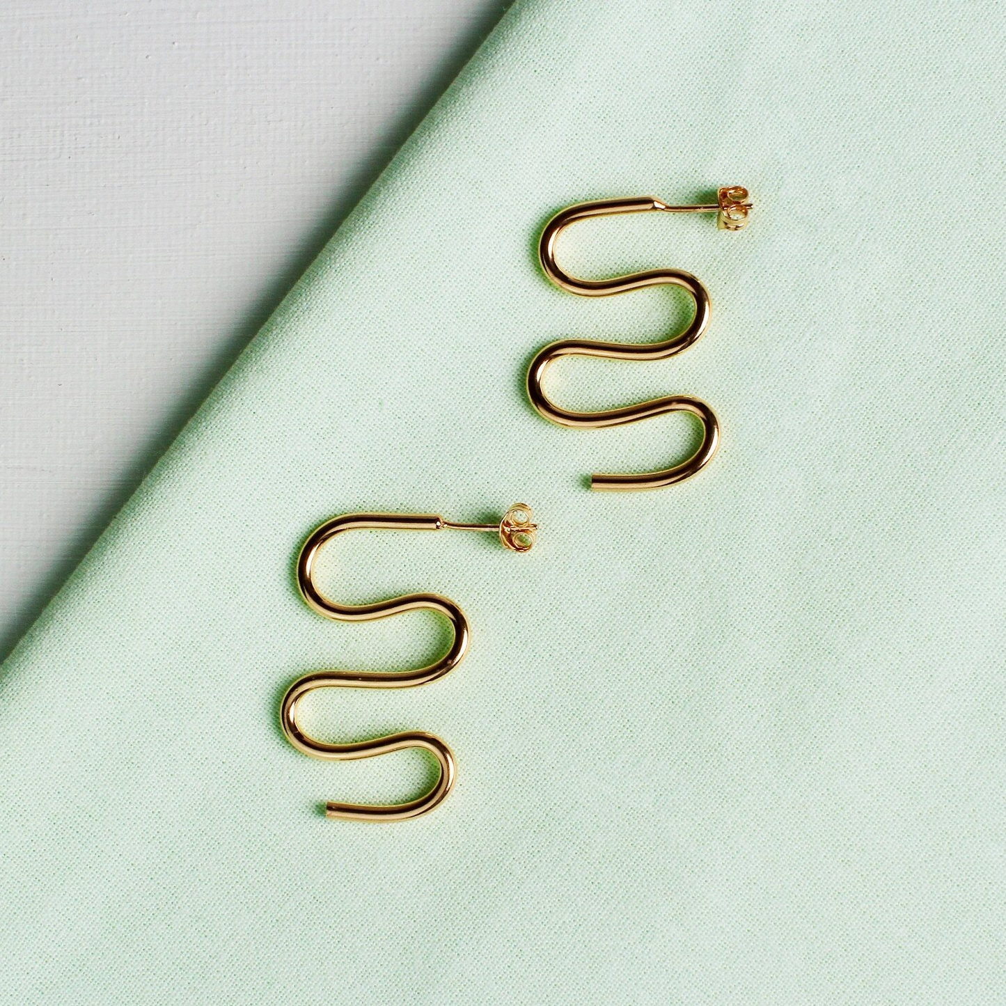 Close up of gold earrings in the shape of a squiggle