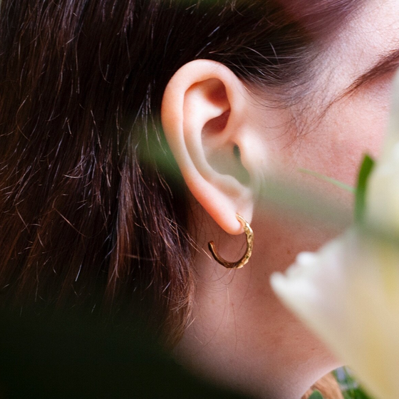 Close up of woman wearing small gold hoop earring with a textured surface